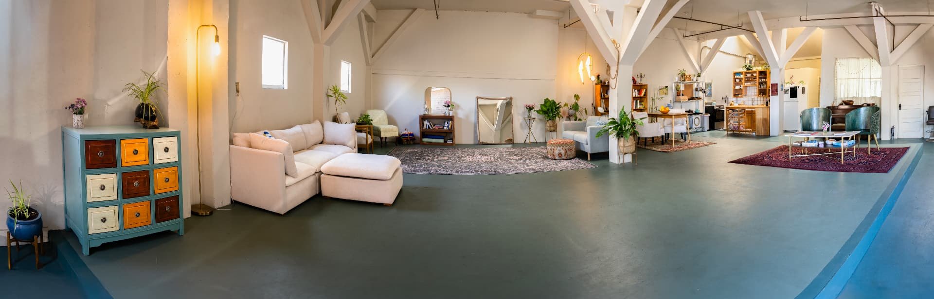 A wide panorama of the Scuttlebutt Studios room: rugs, armchairs, piano and long table beneath whitewashed timber trusses