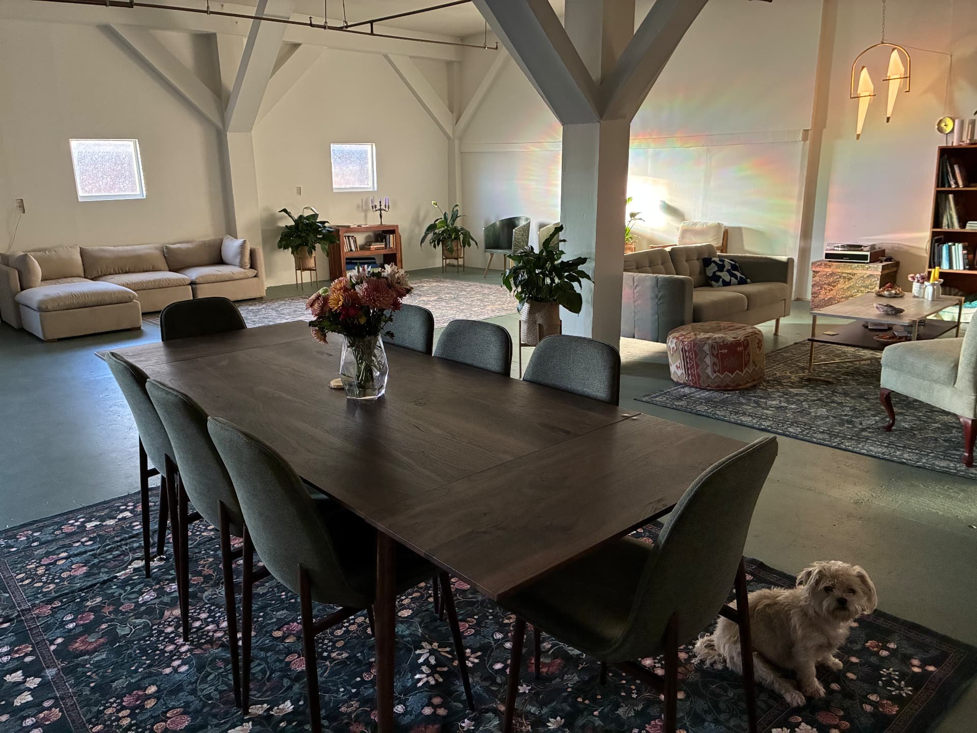 The long dining table and sofas under the trusses, with the house dog waiting on the rug