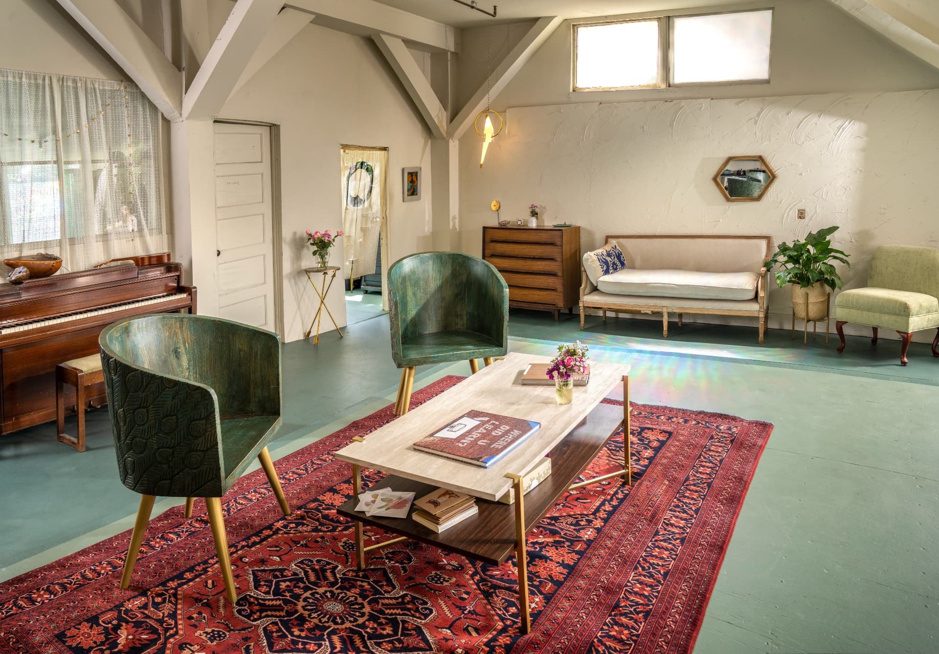 The lounge end of the Harbor with an upright piano, green velvet chairs and a low travertine table on a red rug