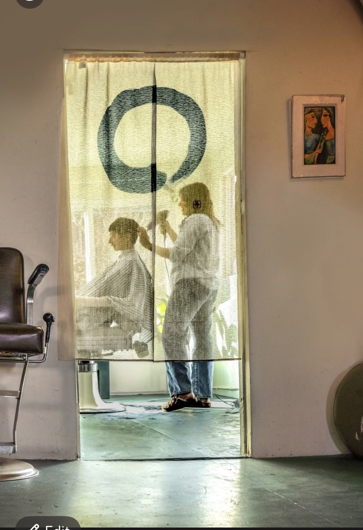 Seen through a linen curtain in the doorway: Natasha working on a client in the private barber room beyond